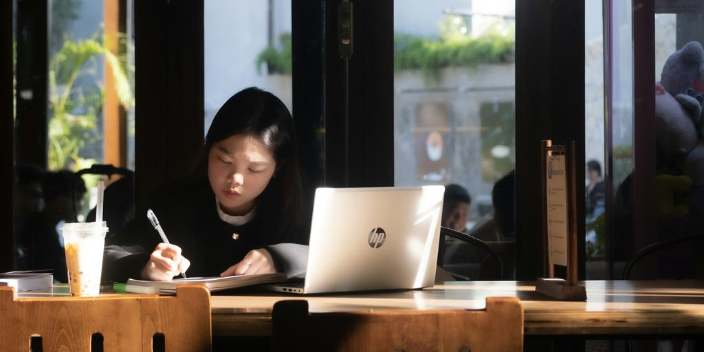 카페에서 노트북을 켜고 노트에 필기하며 공부하는 젊은 학습자, 미래를 위한 배움에 투자하는 소비